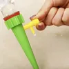 A hand is shown adjusting a yellow valve on a green plant watering spike, with a drop of water falling. Anteprima dell’immagine prodotto