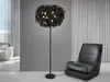 A black feather floor lamp with gold accents is shown in a modern living room setting next to a black leather armchair. Voir les images du produit