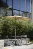 An outdoor seating area with a table, chairs, and an umbrella, set against a building with large windows and lush greenery. Anteprima dell’immagine prodotto