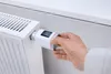 A hand is shown adjusting a smart thermostat on a radiator. Produktbild-Vorschau