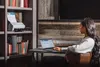 A woman is working on a laptop next to a bookshelf with a printer on it. Voir les images du produit