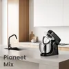 A black stand mixer is shown on a kitchen counter next to a sink. The kitchen has modern white cabinets and wooden accents. Náhled obrázku produktu