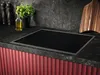 A modern kitchen countertop with a black induction cooktop, a cutting board, a plant, and a bottle of oil. Produktbild-Vorschau