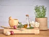 A collection of cooking ingredients and tools on a wooden cutting board, with a potted rosemary plant in the background. Produktbild-Vorschau