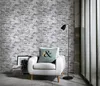 A white armchair with a green pillow sits in front of a brick-patterned wallpaper, next to a floor lamp and a window. Produktbild-Vorschau
