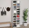 A white shoe cabinet filled with various shoes, bags, and boxes, placed next to a wall with hooks holding a hat and a bag. A wooden bench is in front of the wall, and a large potted plant is to the right of the shoe cabinet. Produktbild-Vorschau