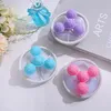 Three laundry balls with mesh bags are arranged on a surface, with a bottle of blue liquid and flowers in the background. Produktbild-Vorschau