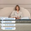 A woman is sitting on a bed reading a book, with pillows behind her. There are informational overlays on the image. Produktbild-Vorschau