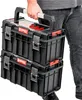 A person is carrying a stack of two black toolboxes. Náhled obrázku produktu