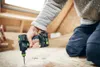 A person is kneeling and using a cordless drill to screw into a wooden floor in an attic. Voir les images du produit