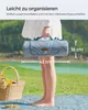 A person holding a rolled-up picnic blanket in an outdoor setting with a lake and trees in the background. Produktbild-Vorschau