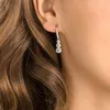 A close-up shot of a woman's ear wearing a pair of dangling earrings. Produktbild-Vorschau