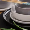 A close-up view of stacked ceramic bowls and plates, with chopsticks resting on top. Green onions are visible in the foreground. Náhled obrázku produktu