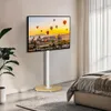 A TV stand with a TV displaying a scenic image, placed in a bedroom setting next to a bed and a plant. Produktbild-Vorschau