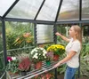 A woman adjusts a vent in a greenhouse filled with plants. Voir les images du produit