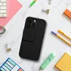 A black iPhone case with a camera cover is placed on a marble surface, surrounded by office supplies. Produktbild-Vorschau