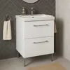 A white bathroom vanity with a sink and two drawers, standing on chrome legs, is shown in a bathroom setting with tiled walls and floor. A towel hangs on a ring to the left, and another towel is draped over the side of the vanity. Produktbild-Vorschau