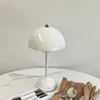 A white mushroom-shaped table lamp sits on a white marble-patterned table, with a box of pens and cutlery in brown packaging in the foreground. Produktbild-Vorschau