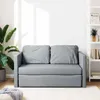 A light gray sofa bed is shown in a well-lit room with a large plant on the left and a white bookshelf on the right. Produktbild-Vorschau