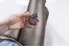 A hand holding a watch over a person's lap. Náhľad obrázku produktu