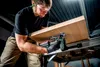 A man is using a cordless jigsaw to cut a piece of wood on a workbench. Produktbild-Vorschau