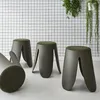 Four khaki-colored stools with green textured seats are arranged in a room with a black and white grid-patterned wall and hanging plants. Produktbild-Vorschau