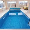 An indoor swimming pool with blue tiled walls and floor, covered with a blue pool cover. Náhled obrázku produktu