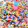 A collection of colorful pom-poms scattered around a phone case decorated with pom-poms and a small pom-pom creature. Produktbild-Vorschau