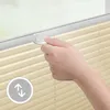 A hand is shown adjusting a cream-colored pleated blind attached to a window frame. Produktbild-Vorschau