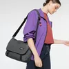 A woman wearing a purple jacket and red shirt, carrying a gray messenger bag. Anteprima dell’immagine prodotto