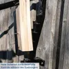A close-up shot of a manual wood splitter mounted on a wooden wall, with a piece of wood being held in place by a nail. Produktbild-Vorschau