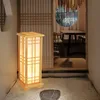 A Japanese-style floor lamp is placed on a gravel floor next to a sliding door that leads to a dining area with a table and chairs. Náhled obrázku produktu