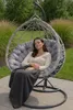 A woman is sleeping in a hanging egg chair outdoors, covered with a blanket. Voir les images du produit