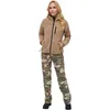 A woman stands against a white background wearing a tan fleece jacket and camouflage pants. Produktbild-Vorschau