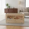 A hamster cage is placed on a rug in a living room setting, with a couch and cabinet in the background. Produktbild-Vorschau