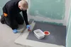 A person is applying a waterproofing compound to a shower floor. Produktbild-Vorschau