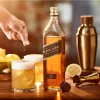 A hand garnishing a cocktail with spices next to a bottle of Johnnie Walker Black Label whisky. Produktbild-Vorschau