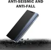 A black phone case with a transparent flip cover is shown at an angle, resting on a dark, cracked surface with scattered rocks. The background is white. Produktbild-Vorschau