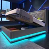 A modern bedroom with a grey upholstered bed frame, featuring integrated LED lighting and storage. The bed is shown with the mattress lifted, revealing the storage compartment underneath. Náhled obrázku produktu