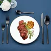 A table setting with a plate of sliced steak, roasted garlic, and cutlery. Podgląd zdjęcia produktu