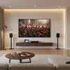 A modern living room with a large TV displaying a concert, a media console, two speakers on stands, and a coffee table with snacks. Anteprima dell’immagine prodotto