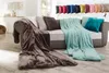 A sofa with several blankets and pillows, with a row of colorful pillows displayed on a shelf above. Produktbild-Vorschau