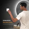 A man is interacting with a light switch next to a backlit mirror in a bathroom. Produktbild-Vorschau
