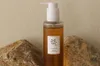 A bottle of cleansing oil is placed between two rocks against a textured beige background. Anteprima dell’immagine prodotto