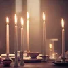 Several lit white taper candles are arranged on a wooden table, with bowls and other decorative elements in the background. Podgląd zdjęcia produktu