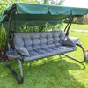 A garden swing with a green canopy and gray cushions, set on a grassy lawn with tall plants in the background. Produktbild-Vorschau