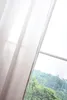 A sheer curtain is partially drawn across a window, revealing a lush green hillside outside. Produktbild-Vorschau