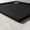 A close-up, angled view of a black shower tray with a silver drain cover. Produktbild-Vorschau