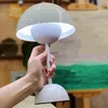 A hand holding a white mushroom-shaped desk lamp with a light on. Produktbild-Vorschau