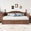 A wooden daybed with drawers, set up in a bedroom with decorative pillows and framed pictures on the wall.